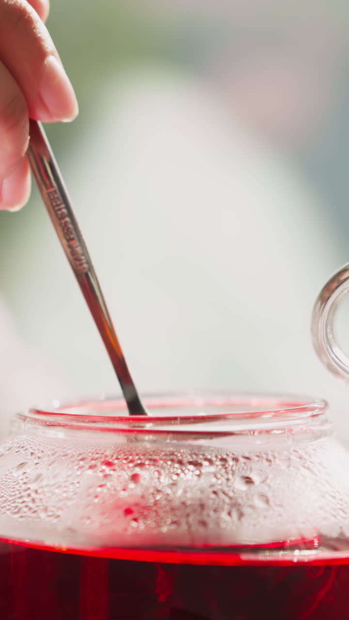 한 여인이 컵과 함께 유리 비에 차를 니다. 여자는 식탁에서 아침 식사를 위해 뜨거운 허브 음료를 준비합니다. 향기있는 히비스쿠스 음료를 양조하는 과정