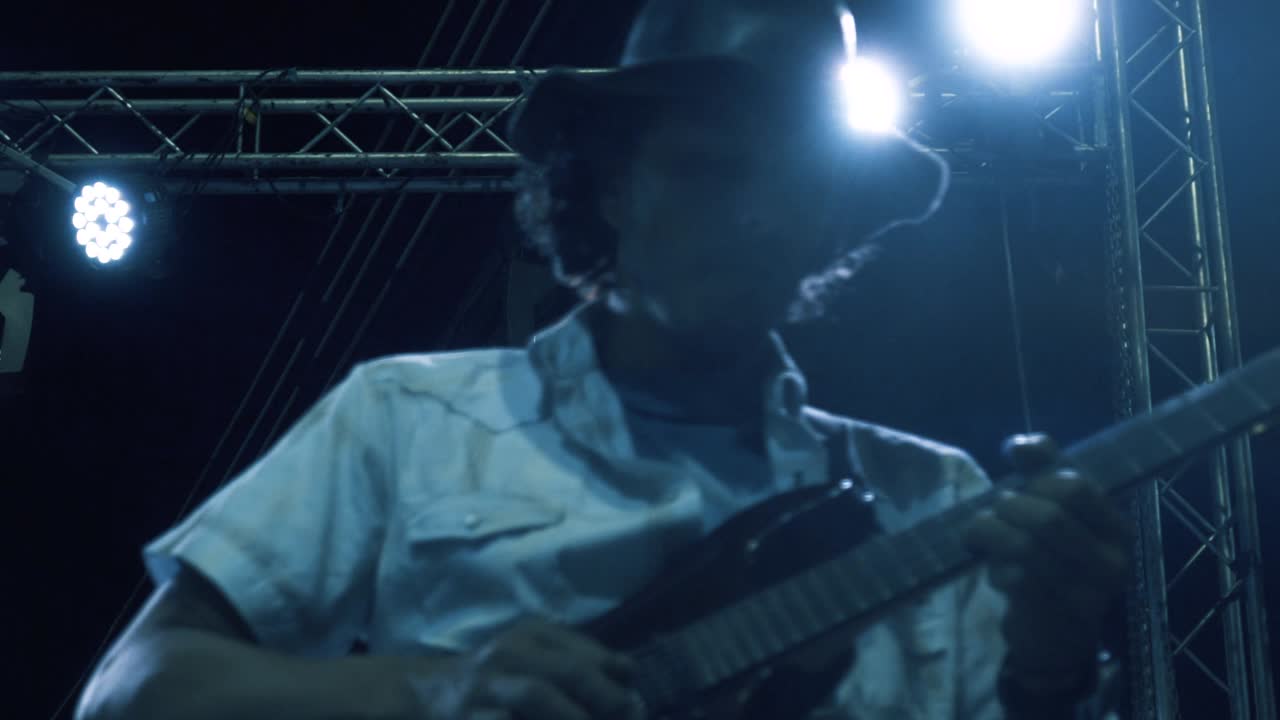 Close-up dalam gerakan lambat seorang gitaris membawakan lagu di konser malam terbuka
