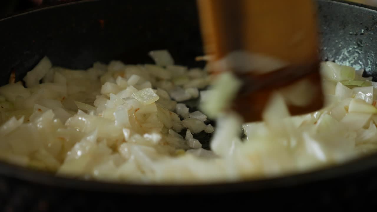 Frying onions in a pan with oil. Stir onion in skillet with wooden spatula