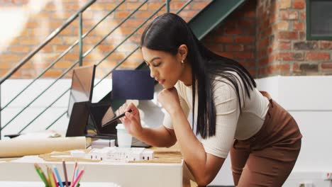 Thoughtful-biracial-female-architect-looking-at-architectural-models-at-office