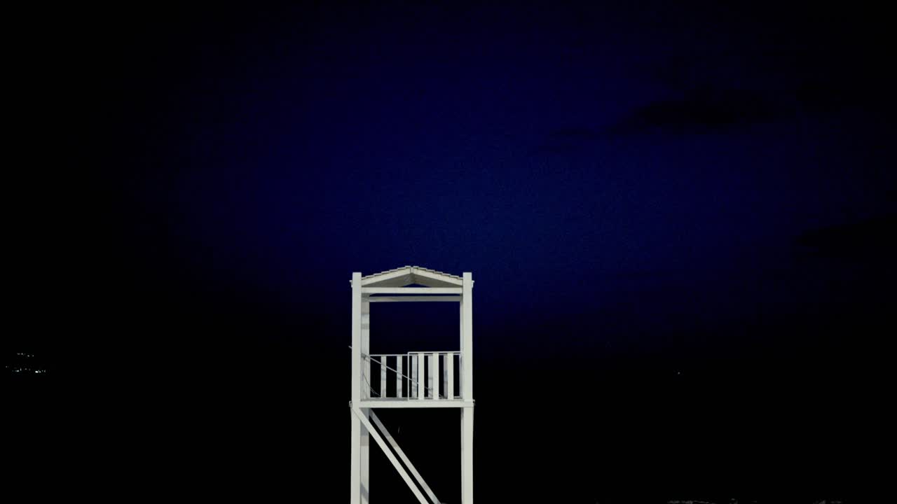 Tilt down revealing shot of life guard tower and boat, at beach of Kalamata, night footage 4K