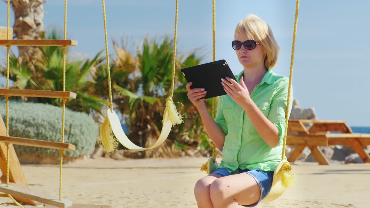 женщина-туристка наслаждается планшетом, сидя на качелях