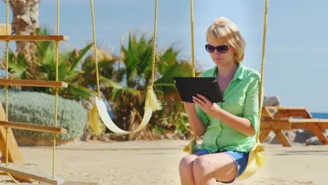 a female tourist enjoys the tablet sitting on a swing