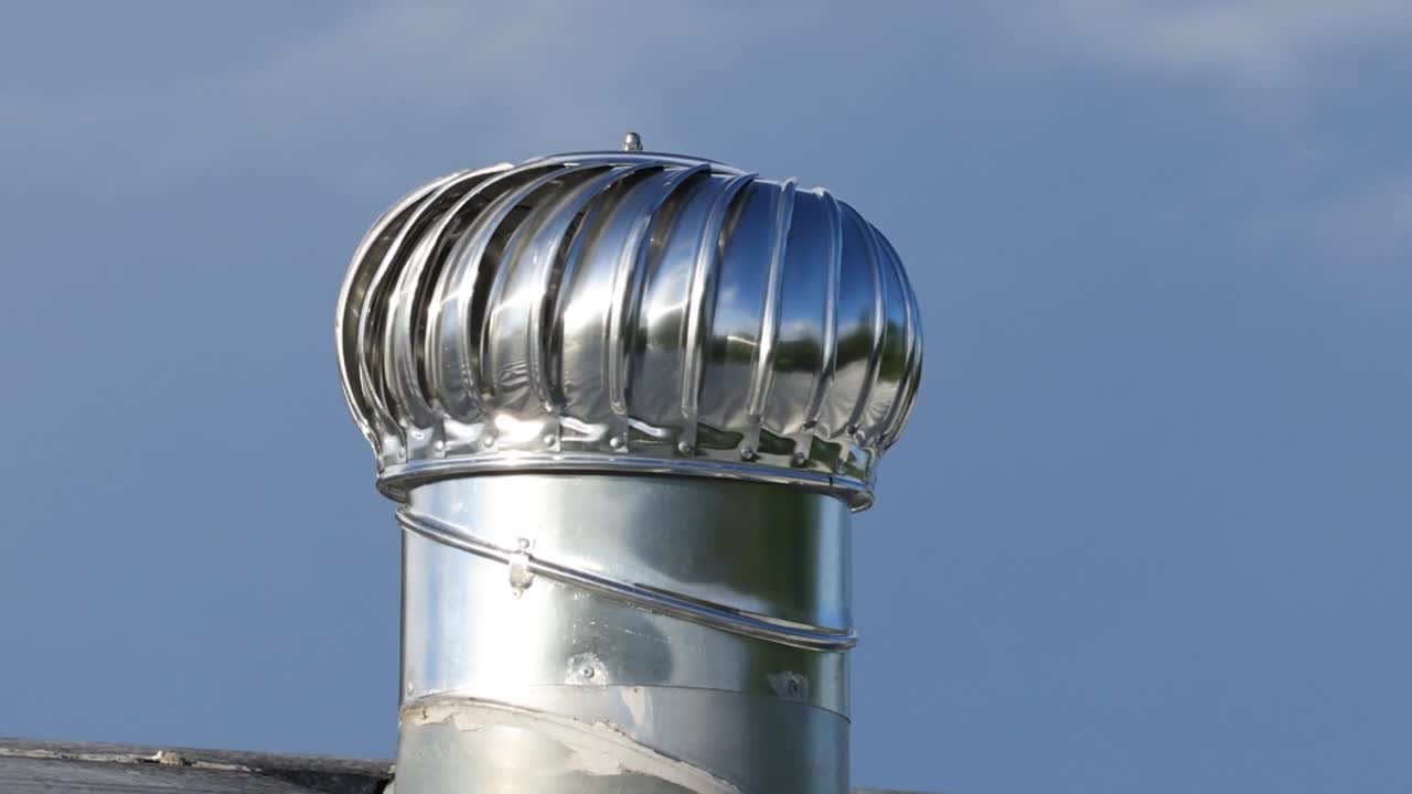 Detailed view of a shiny metal ventilation turbine spinning under a clear blue sky.