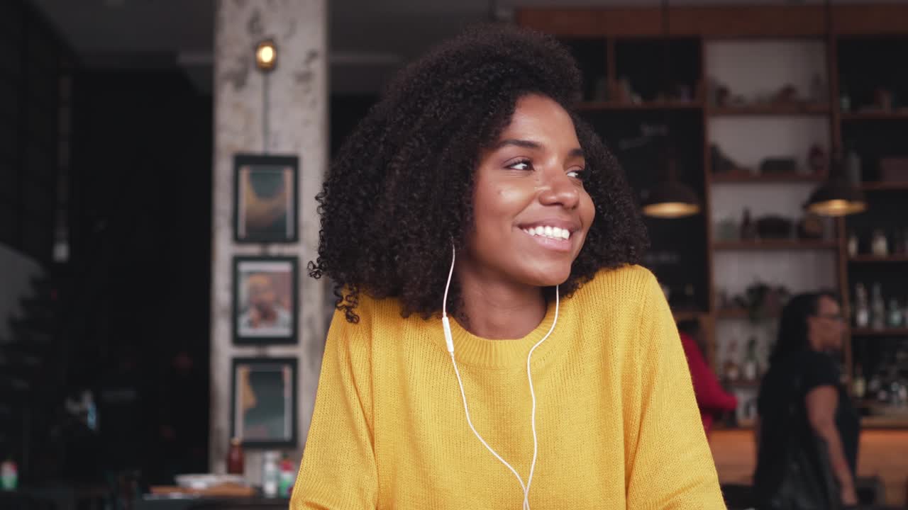 Giovane donna sorridente che ascolta musica con gli auricolari in un caffè.
