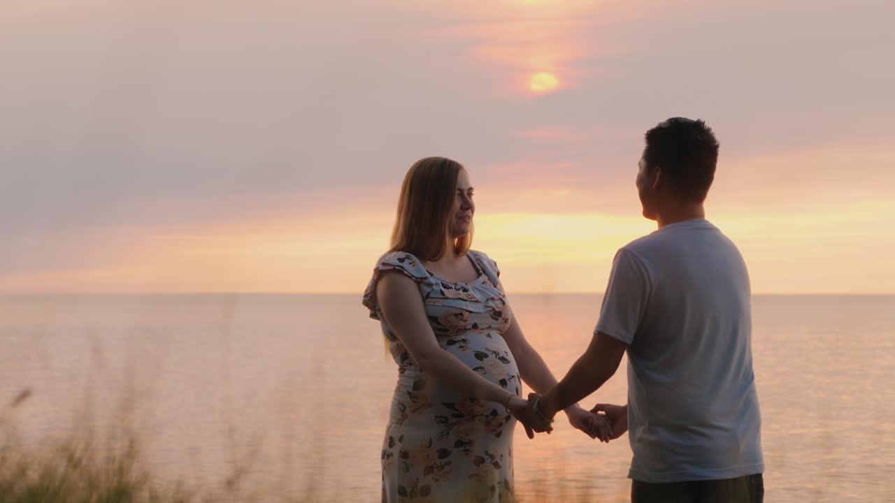 다민족 몰트 커플이 바다 위의 일몰을 배경으로 손을 잡고 있다.