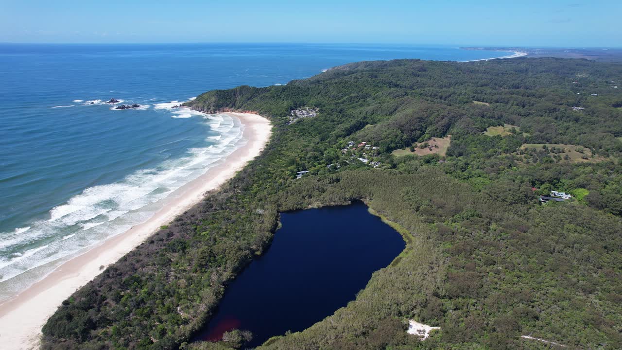 Broken Head Beach With Lagoon Surrounded By Forest Trees In New South Wales, Australia. aerial pullback shot