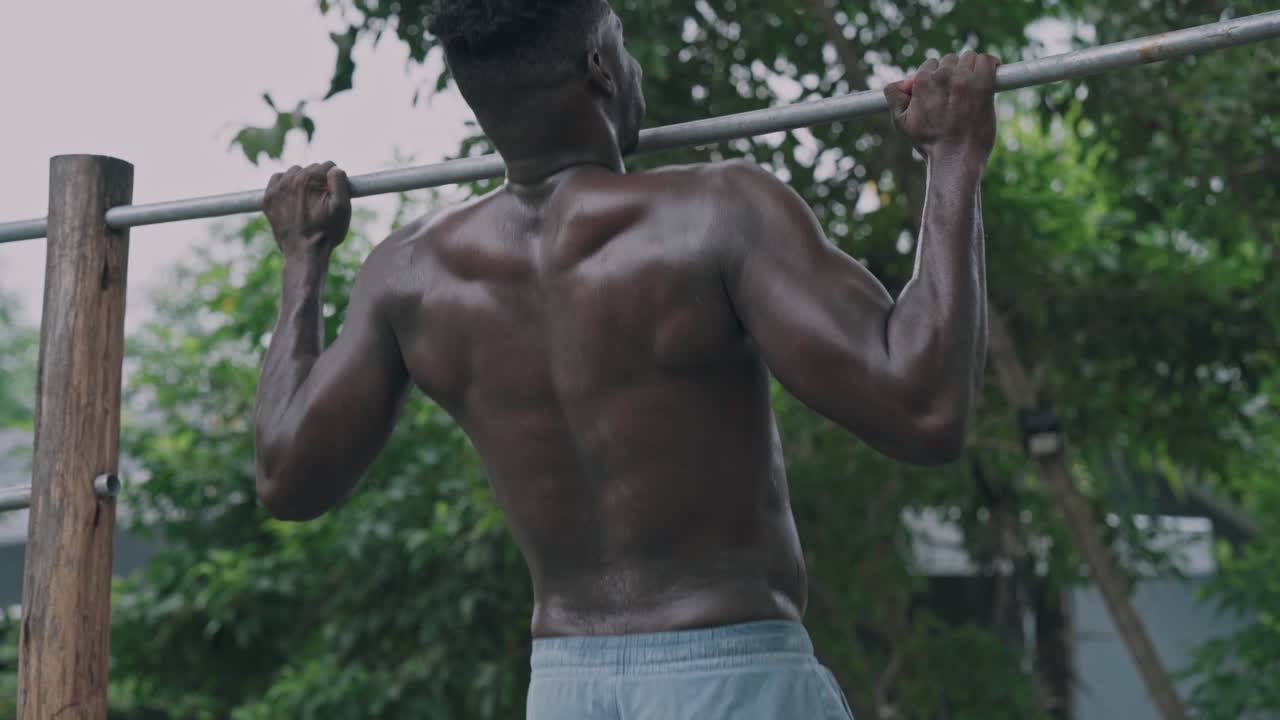 Muskuløs sort mand laver pull-ups i udendørs fitnesscenter