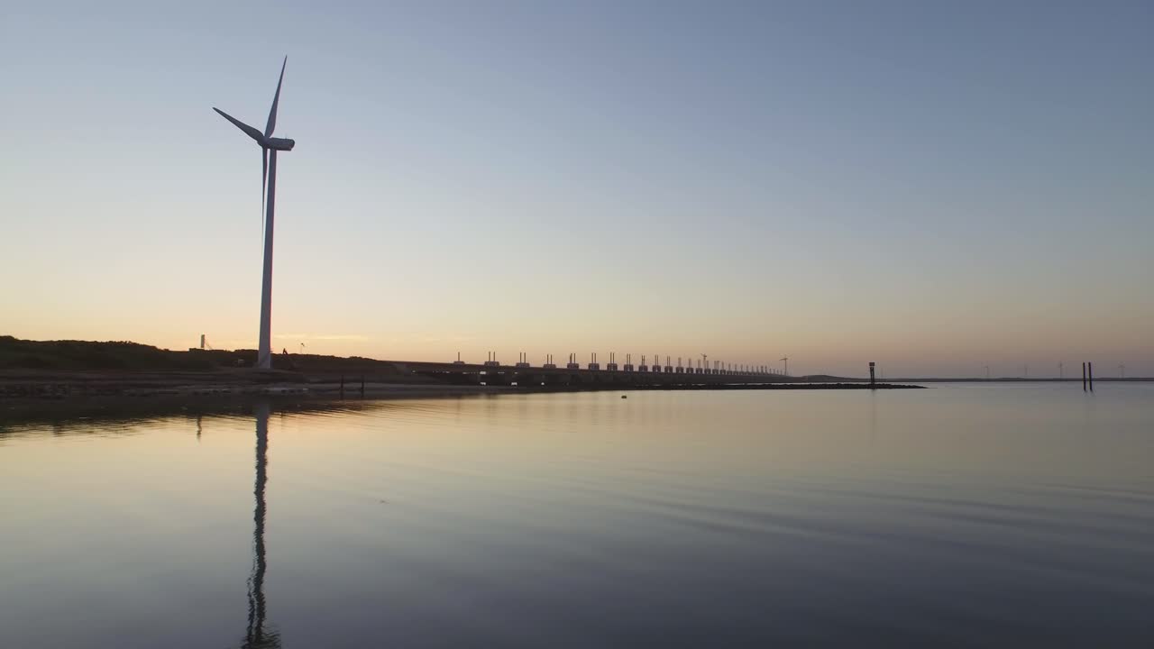 Wind turbines and a long dam reflecting in the water at sunset