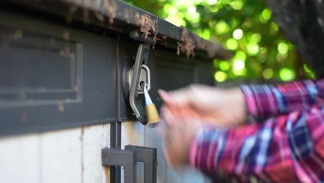 Beautifully-shot-close-up-of-an-open-padlock-and-latch-on-a-shed-with-hands-reaching-in-to-close-the-latch-and-replace-the-lock,-with-stylish-bokeh