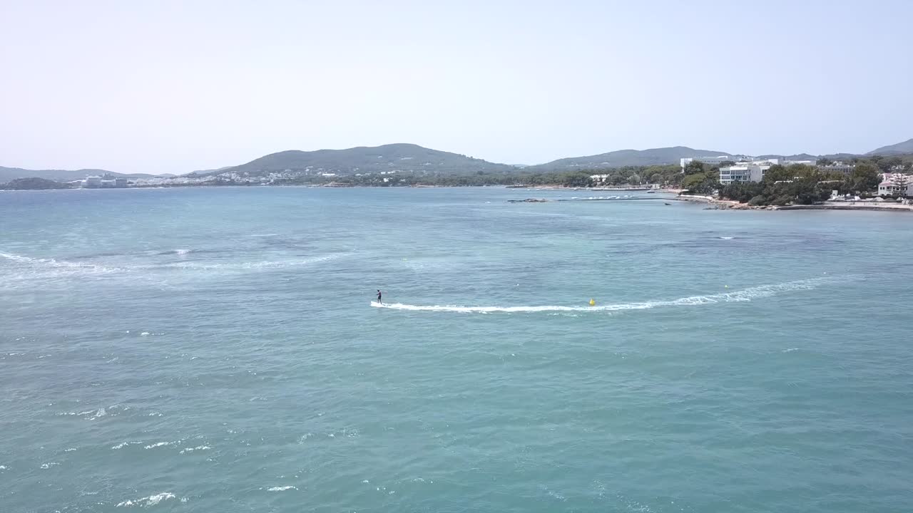 Aerial Orbit Shot around a surfer surfing an electric surfboard, on the Turquoise Coasts of Santa Eularia - Ibiza