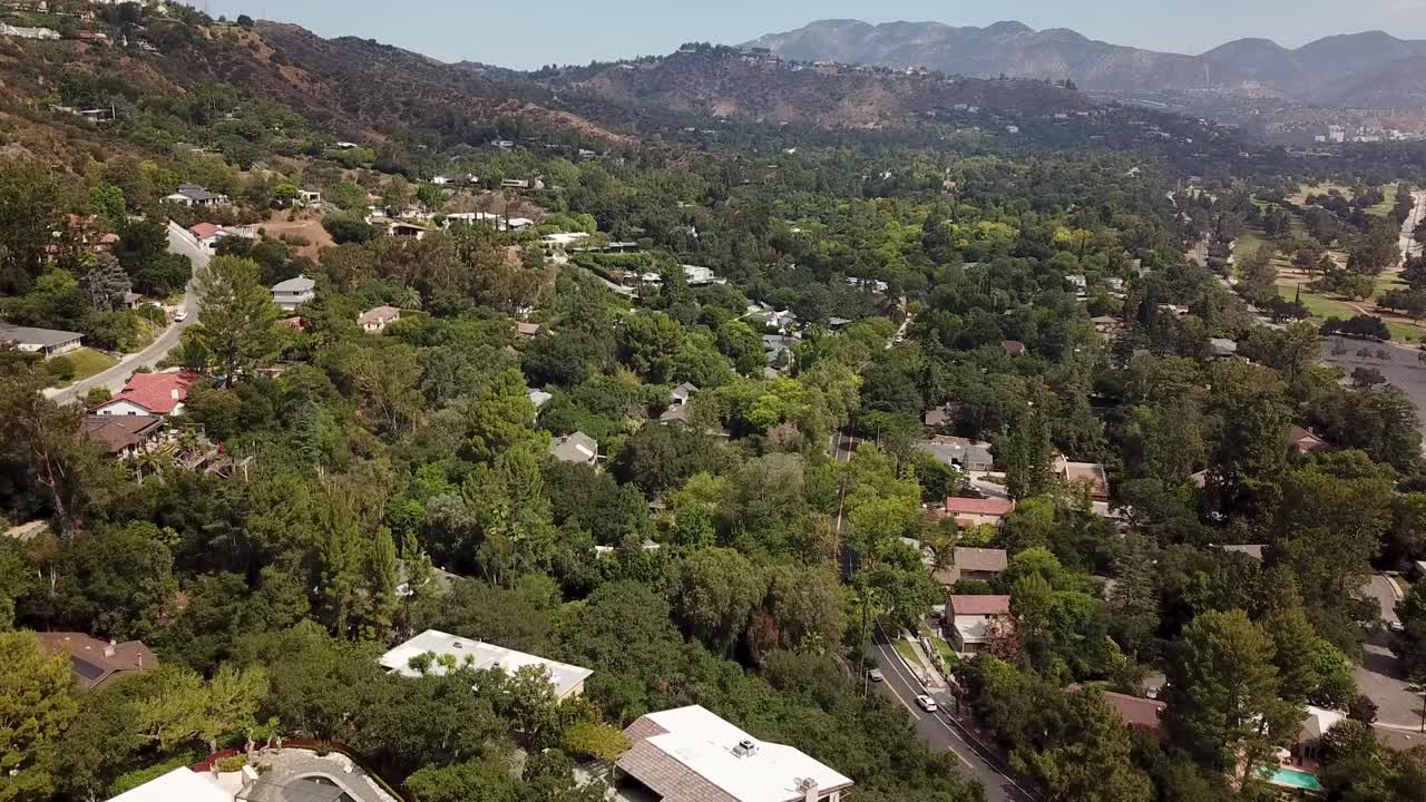 Houses and homes between green trees on hill in Pasadena, California. Aerial flyover shot. Sunny day in suburbia of Los Angeles