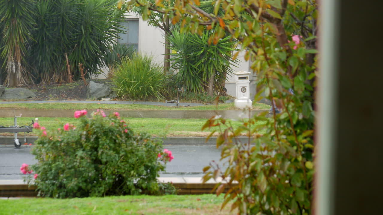 빨간 우산과 회색 비옷을 입고 폭우 속에서 교외 거리를 걷는 남자