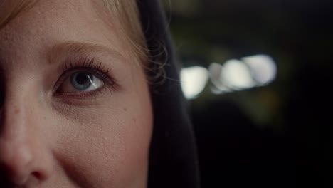 blonde woman open blue eyes at night, white light background, closeup