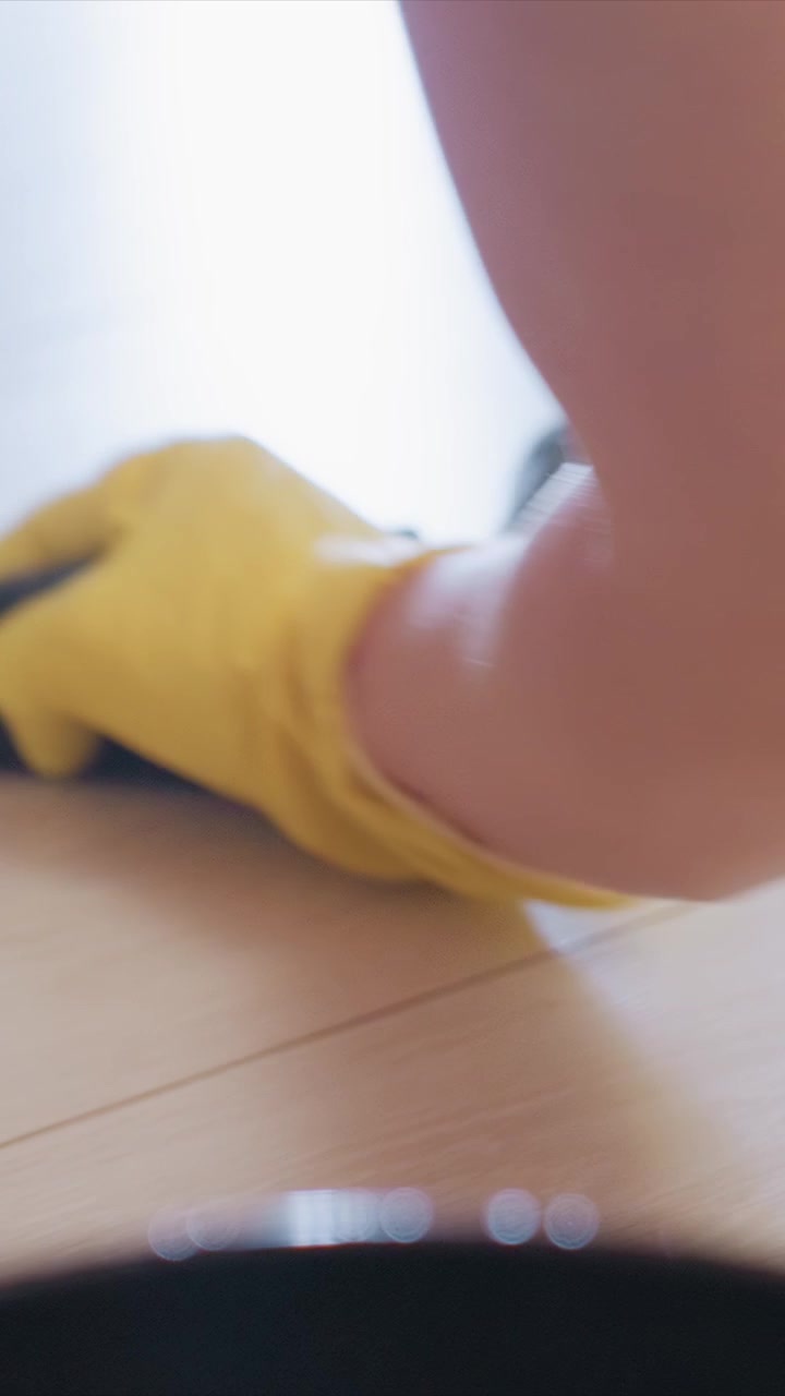 Perspective shows person gloved hands methodically moving across light colored wooden floor. arm and hand in yellow gloves repeatedly sweep wipe or scrub to clean surface