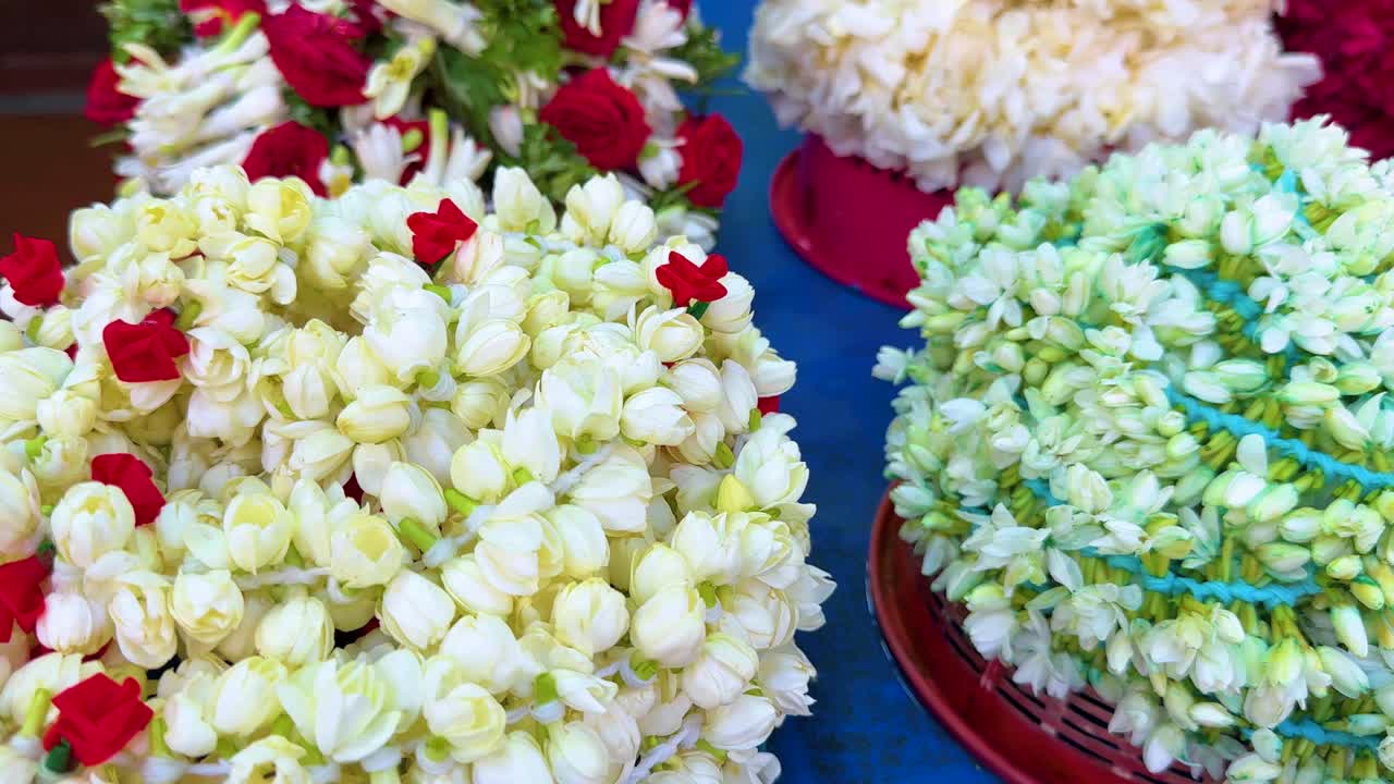 Colorful jasmine and rose flower garlands arranged on a blue table, captured in bright daylight with a smooth lateral camera pan in a Singapore market