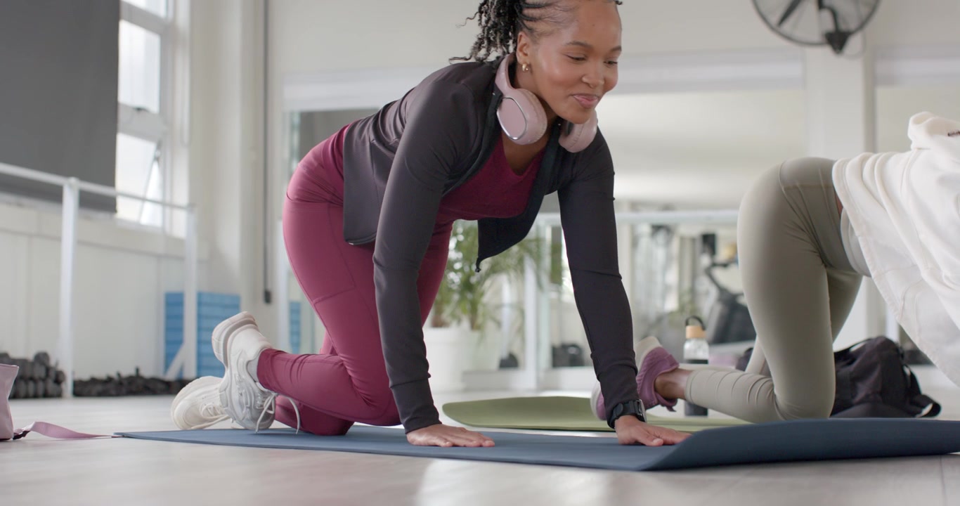 African women in gym clothes entering gym placing mats, unrolling, kneeling preparing workout