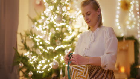 smiling woman wraps presents by the christmas tree