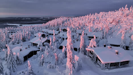 vista aérea sobre cabañas nevadas y árboles rosados en la cima de una montaña en laplandia