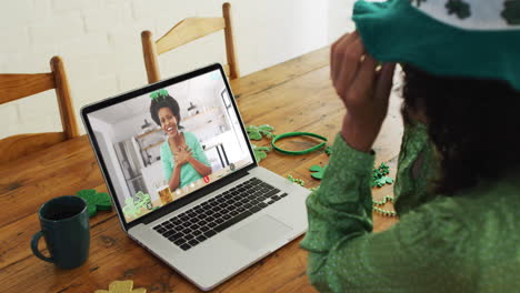 mujer afroamericana sonriente con cerveza vistiendo banda en forma de trébol en una llamada de video en una computadora portátil