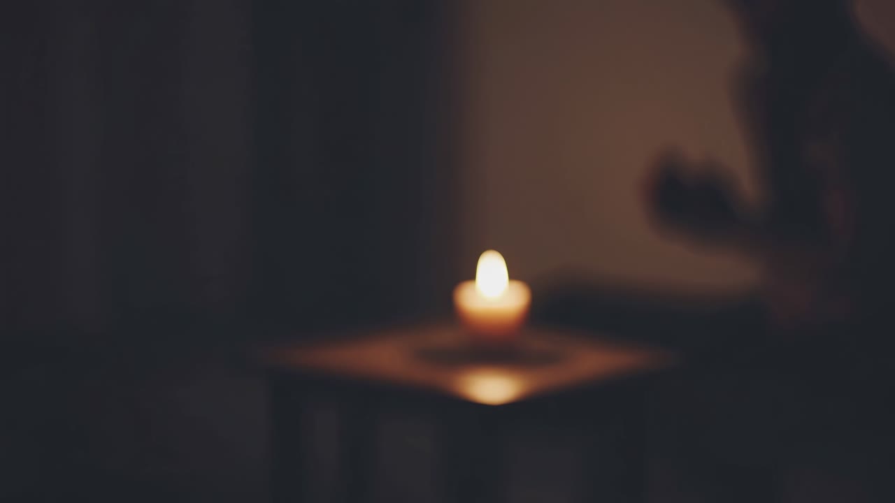 A dimly lit video scene with a blurred candle on a table