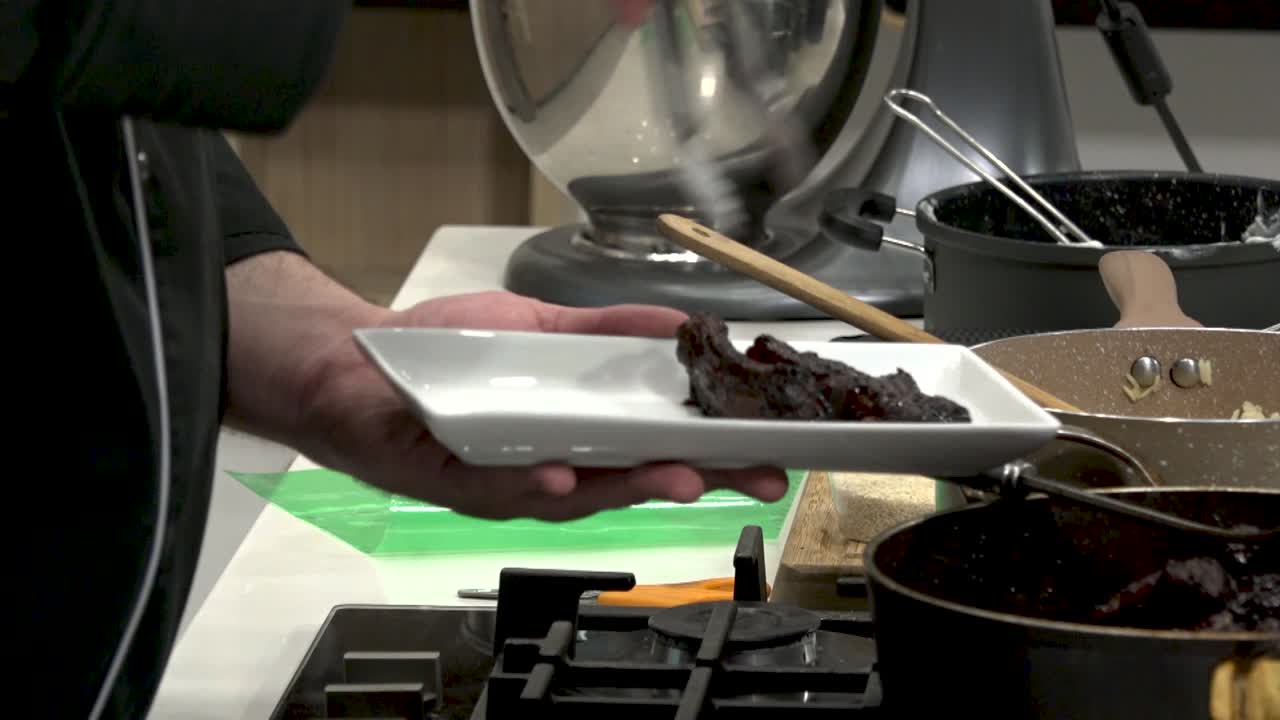 In a contemporary kitchen, a chef skillfully serves a rich dessert from a pot onto a sleek plate, showcasing culinary techniques and flavors in action.