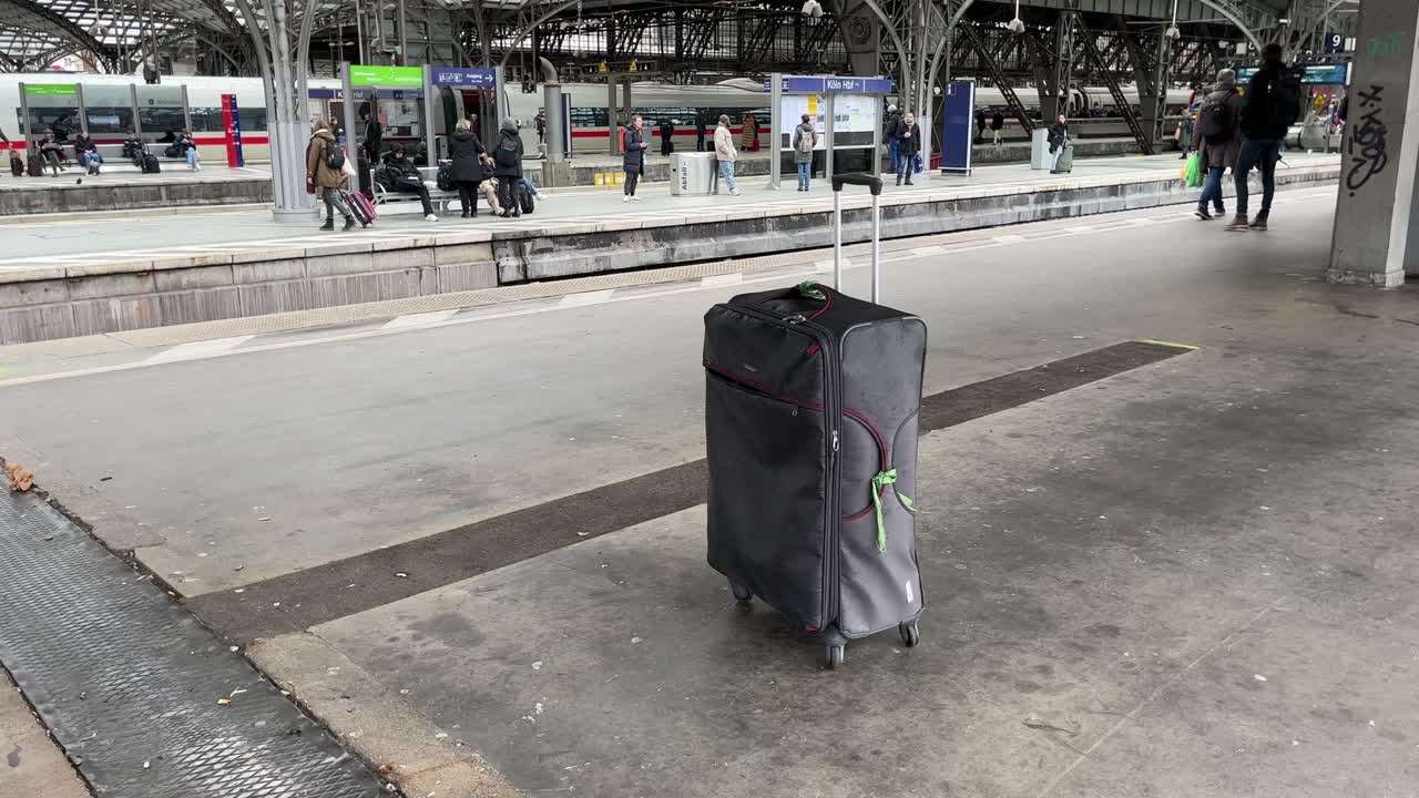 Gray suitcase with a green ribbon stands alone on a train platform without an owner