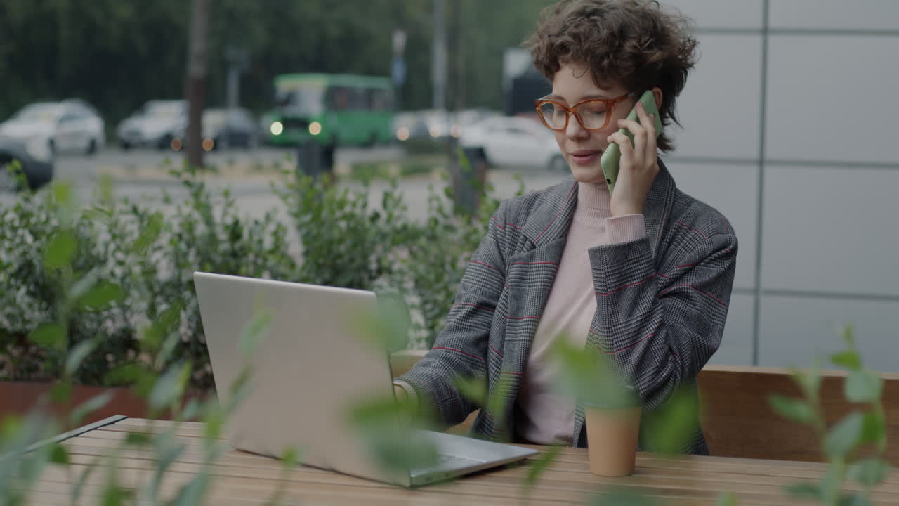 Kvinde arbejder udendørs på en bærbar computer og taler i telefon