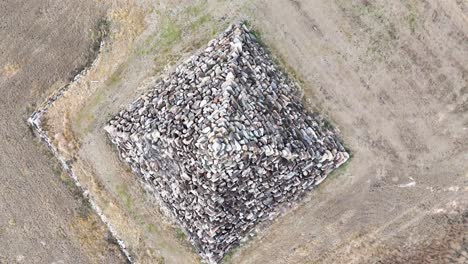 a drone camera smoothly ascends above a large stone pyramid structure in a dry, open field near ballandean, queensland, under diffuse daylight