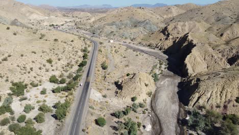 aerial drone zoom in shot over a vehicle parked alongside a winding rcd road surrounded by arid vegetation in balochistan at daytime