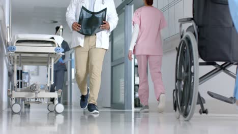 Biracial-male-doctor-walking-with-x-ray-scan-in-hospital-corridor,-slow-motion