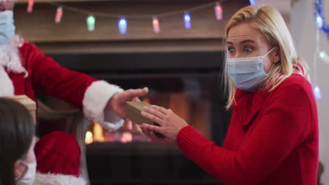 Santa-Claus-wearing-face-mask-giving-the-gift-box-to-mother-and-daughter
