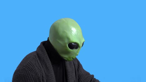 old retired alien in warm knitted jacket instructively raises index finger in the air and nods his head against blue chromakey background. themed costume for party