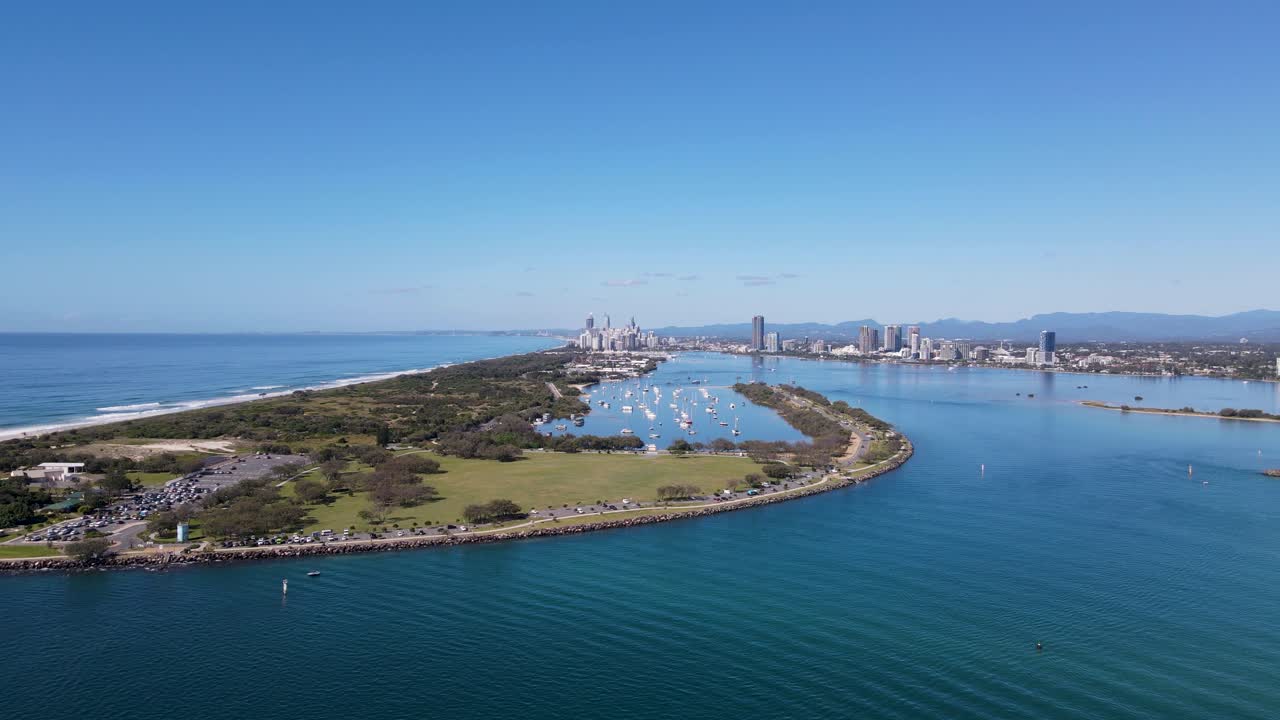 멀리 대도시 스카이라인과 산맥이 보이는 인공 바다 입구와 안전한 보트 항구의 높은 정적 드론 전망