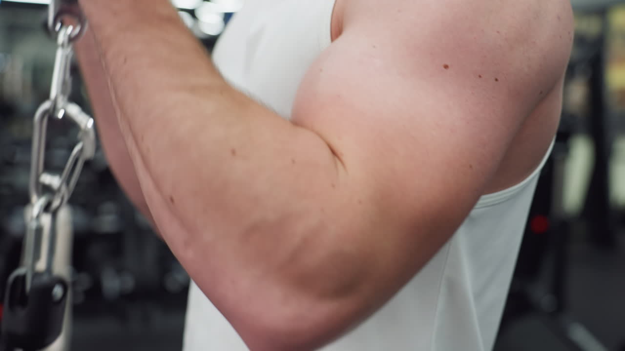 Bodybuilder flexes defined arm while powering cable machine curls in spacious modern gym, veins surfacing and triceps pumping with focused strength during intense upper body workout