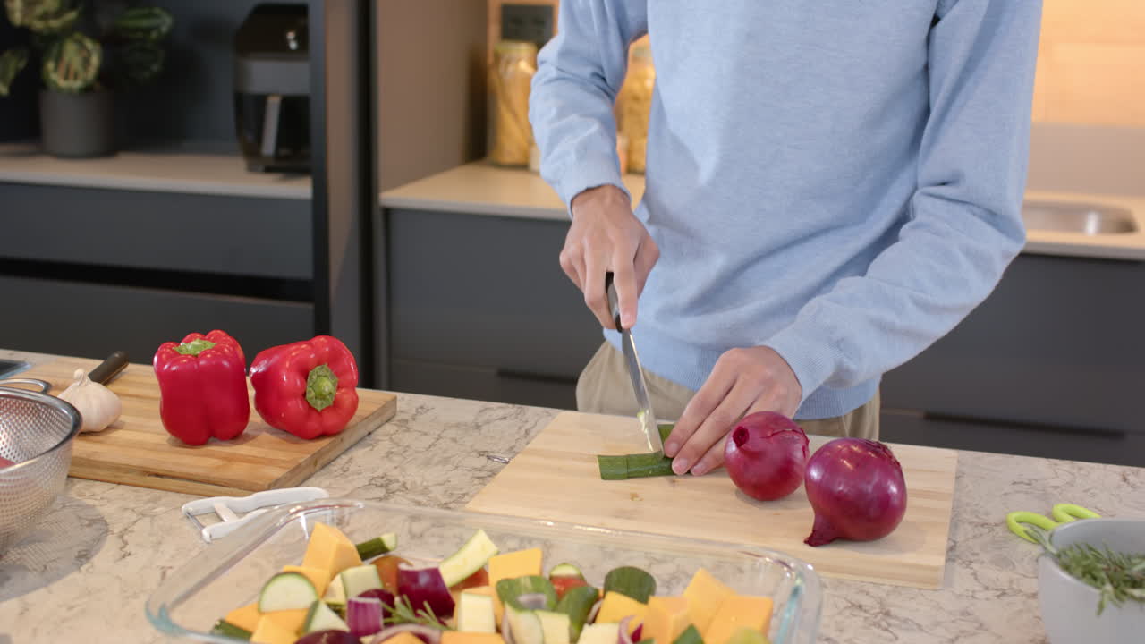 Chopping vegetables on cutting board, man preparing meal in modern kitchen, at home
