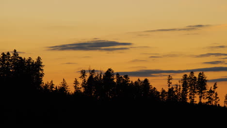 view of the hilltops where dark trees are hidden in the background of shadows and silhouettes of clouds moving on the horizon during sunset