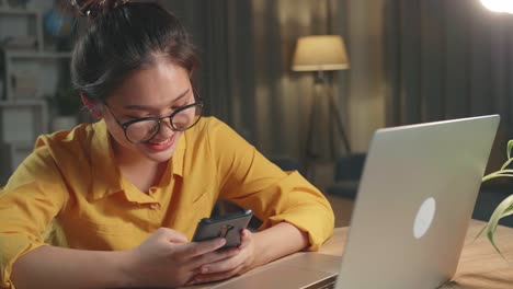 young asia woman use smartphone while working from home at living room at night