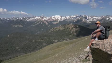 man enjoys mountain peak view from rock on barren grass plateau