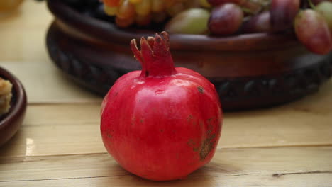 red pomegranate with bee on skin with bowl of fresh grapes in background