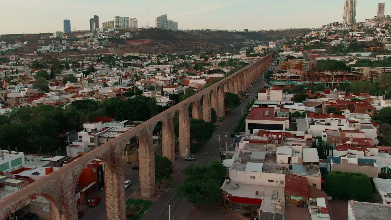 Querétaro, Bajío, Messico - Un lungo acquedotto in pietra si inarca su un quartiere, con case e strade sottostanti - Ripresa con drone in orbita