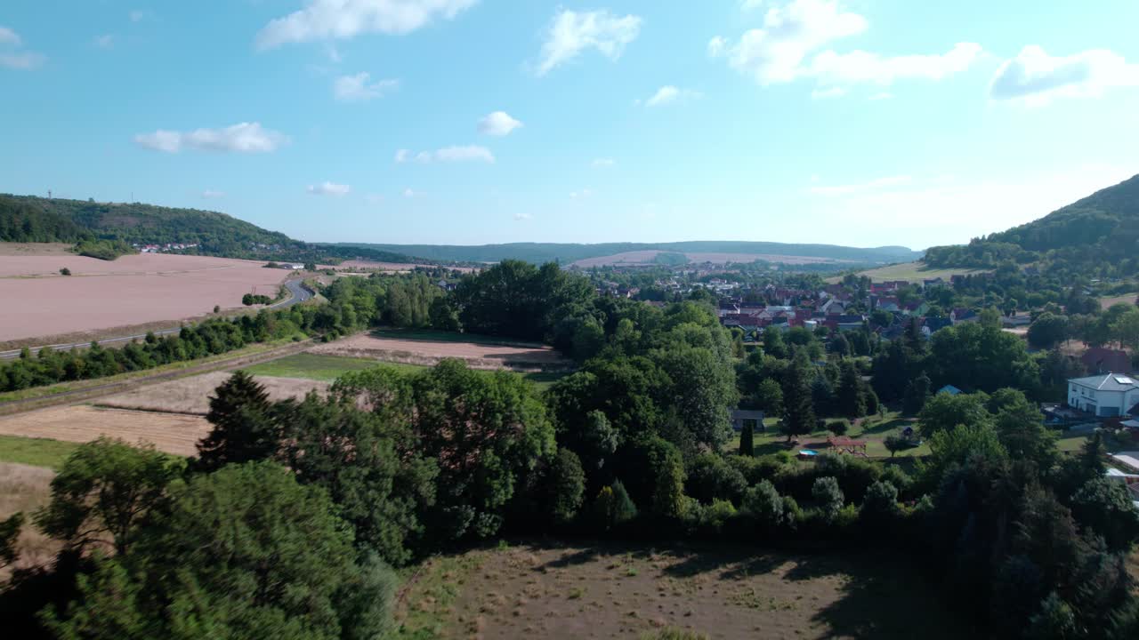 Přelet nad stromy s výhledem na začátek vesnice Sondershausen za letního dne
