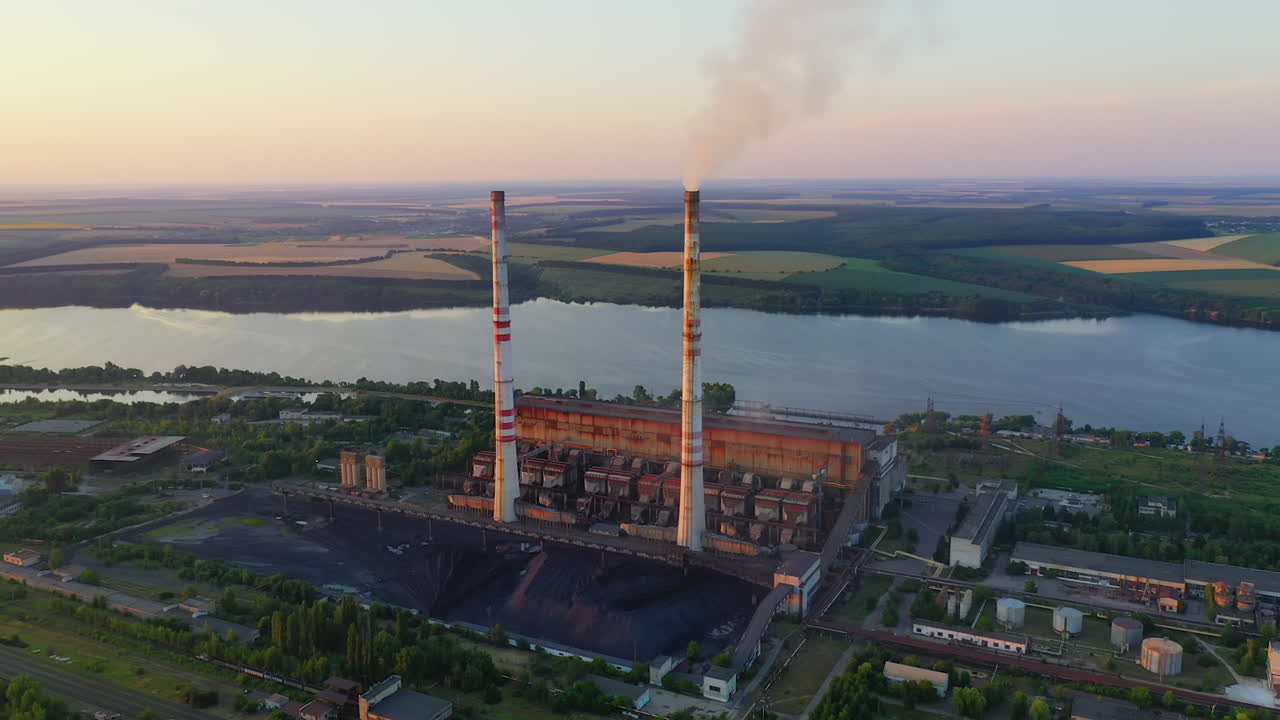 Industrial enterprise on nature background. Chemical plant with pipes near the river. Dirty smoke pours into the air from factory. Environmental pollution. Aerial view