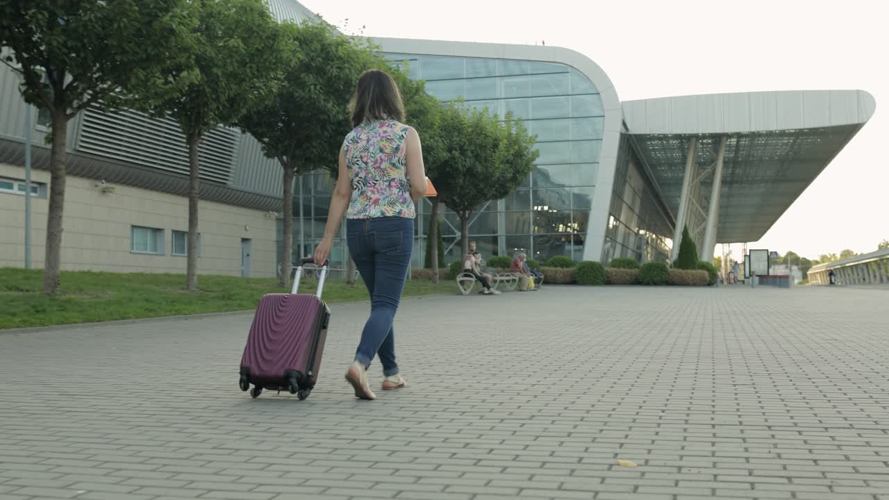 Donna d'affari viaggiatrice che cammina con il bagaglio verso l'aeroporto. La ragazza cammina e trascina la valigia. Turismo.