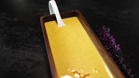 creamy pumpkin soup in a wooden square bowl decorated with flower and herbs on a black table - revealing dolly shot