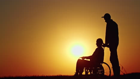 sunset silhouette of a man and a woman in wheelchair