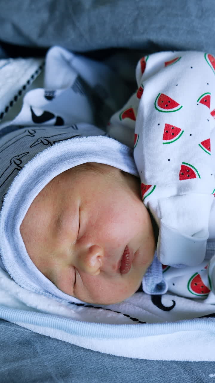 Lovely newborn Caucasian baby sleeping on the bed wrapped in blankets. Top view. Close up. Vertical video