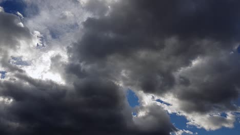 vibrant sunlight hiding behind dark grey clouds moving in blue sky - low angle, time lapse