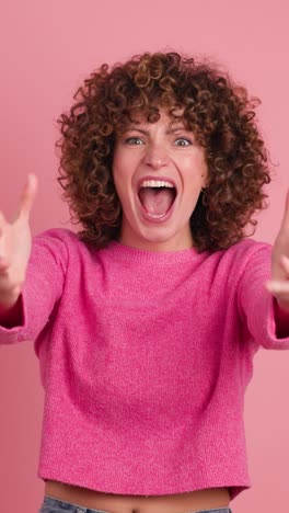 shocked young woman showing stretched hands with palms on pink background. vertical footage