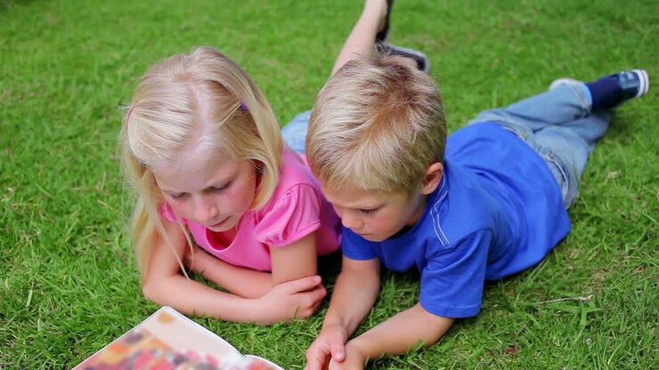 Fratello e sorella leggono un libro sdraiati sull'erba